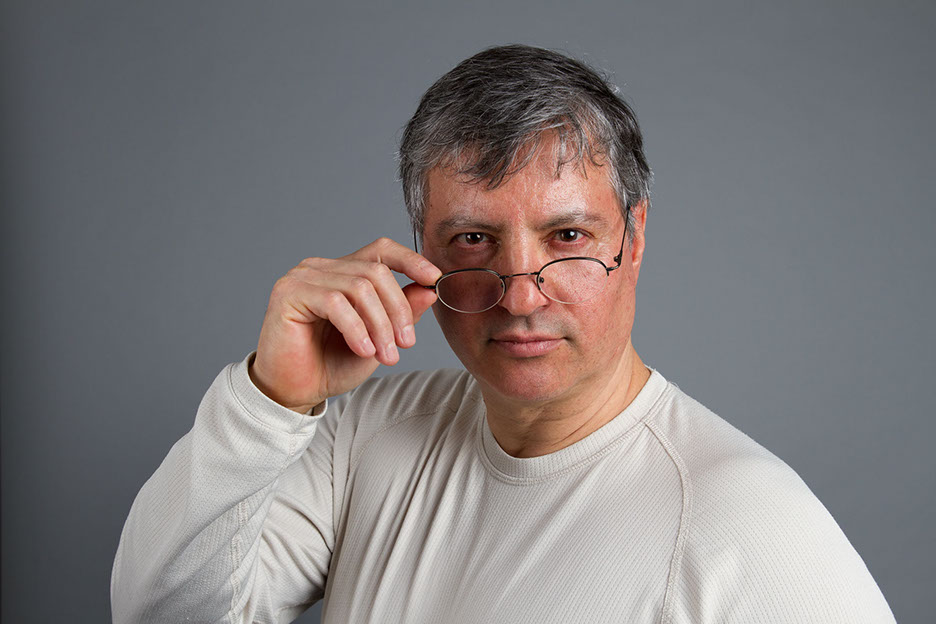 Innenaufnahme von Sergio   Studioaufnahme mit Sergio. Person steht vor einer Neuralen Wandund schau über seine Brille hinweg.