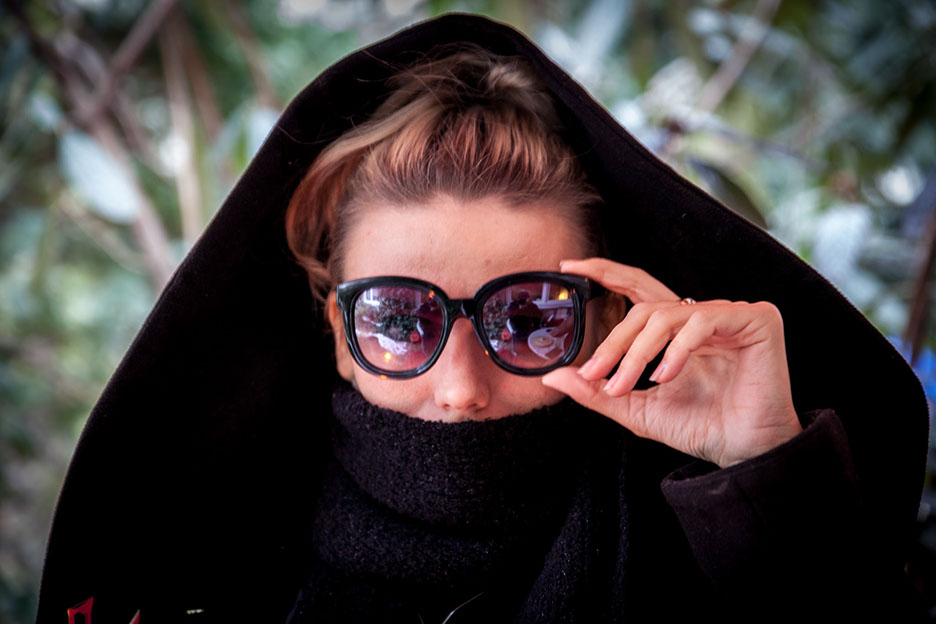 Sunglasses Arina  Arina legt Ihre Hand auf Ihre Sonnenbrille und schaut zur vierten Wand.